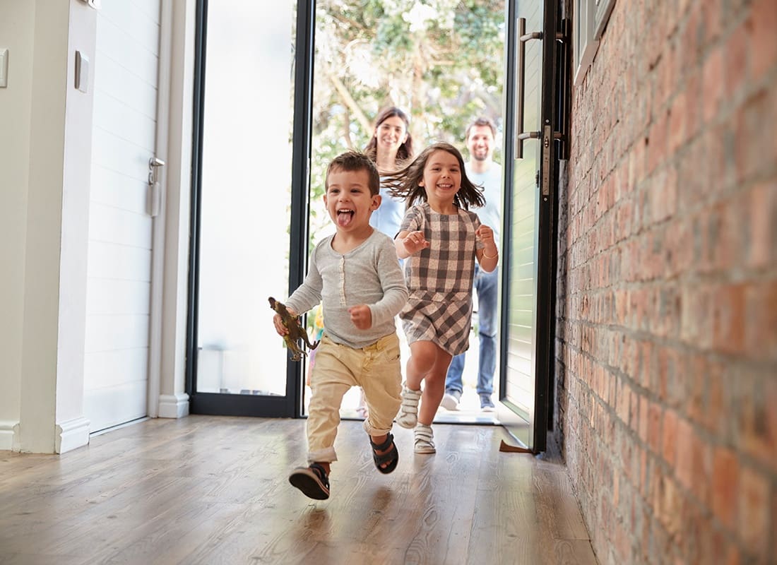 Personal Insurance - Cheerful Young Kids Running Through the Front Door of the House with Their Parents Right Behind Them