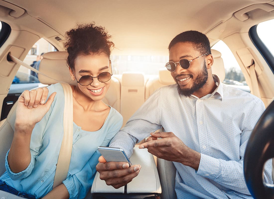 Service Center - Portrait of a Cheerful Young Couple Wearing Sunglasses Sitting in the Car During a Road Trip While Looking at a Phone