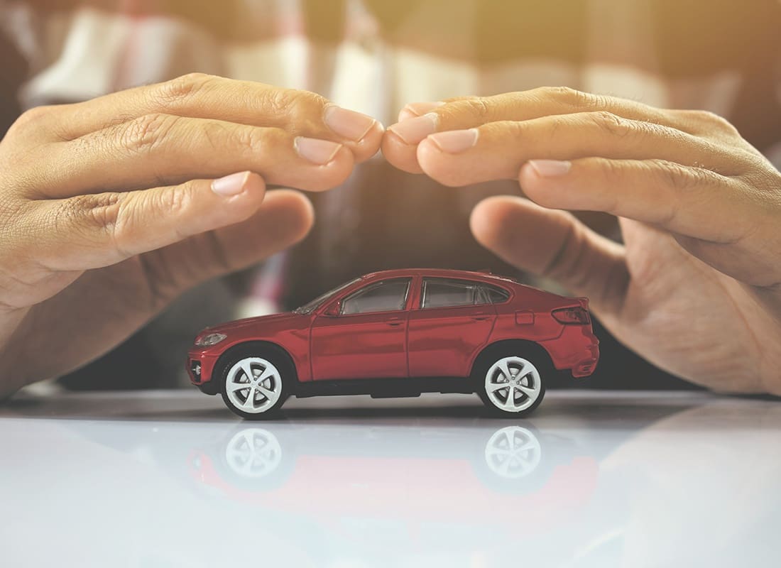 Depreciation Protection Insurance - Closeup View of a Man Holding his Hands Over a Small Red Car on a Table in Protection Concept