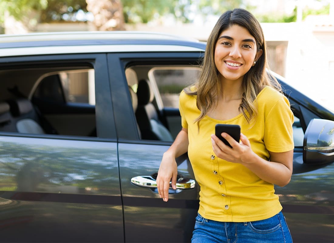 GAP Insurance - Portrait of a Smiling Young Hispanic Woman Standing Next to her Car While Holding a Phone in her Hands