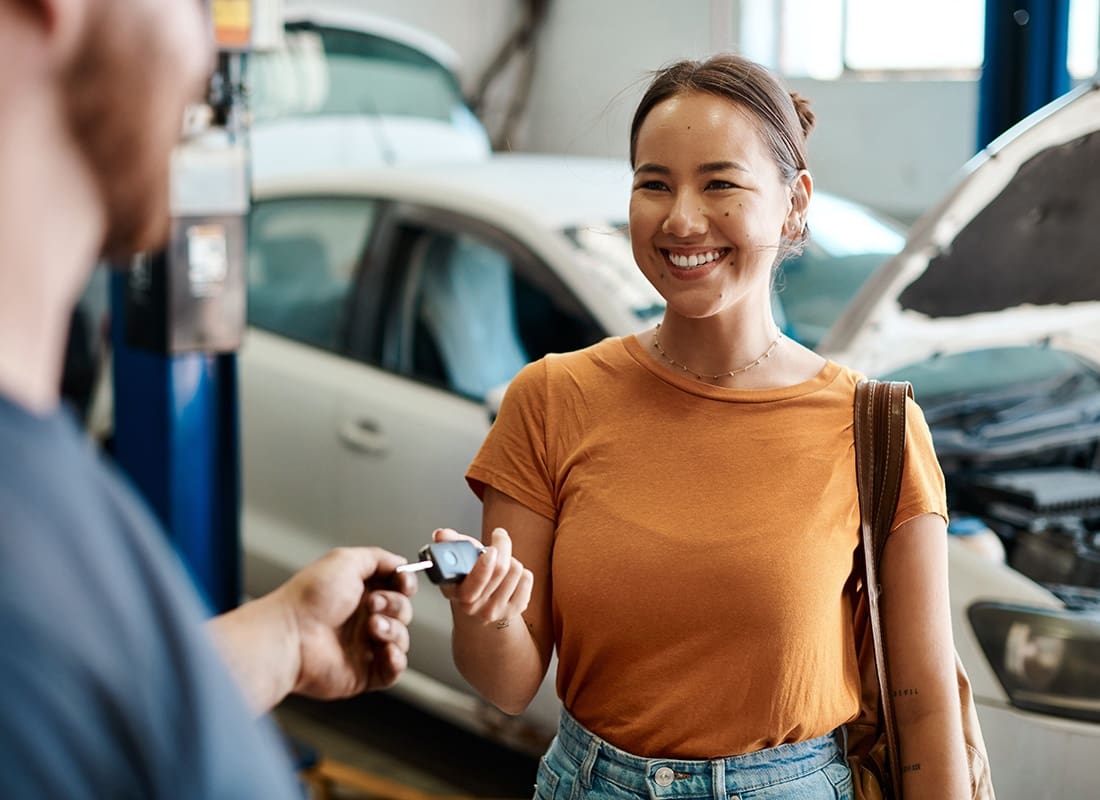 Mechanical Breakdown Protection Insurance - Smiling Young Asian Woman Handing her Car Keys to a Young Mechanic at a Garage Repair Shop