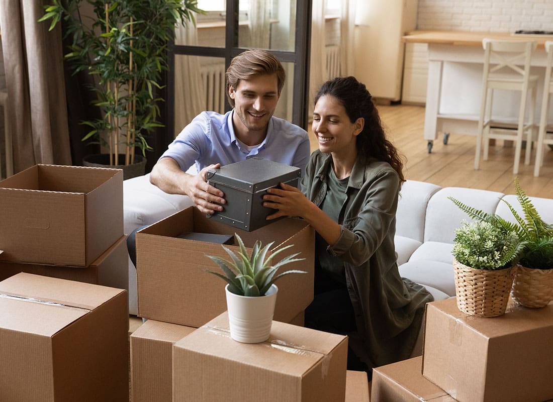 Payment Protection Insurance - Young Married Couple Holding a Safe Box While Sitting Next to Moving Boxes in Their New Home